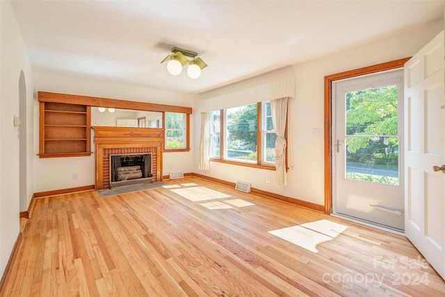 unfurnished living room with a wealth of natural light, a brick fireplace, and light hardwood / wood-style floors