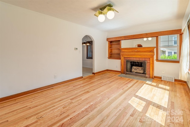 unfurnished living room featuring a brick fireplace and light wood-type flooring