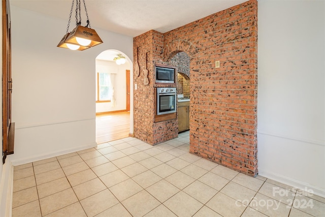 interior space featuring light tile patterned floors, stainless steel oven, black microwave, brick wall, and decorative light fixtures