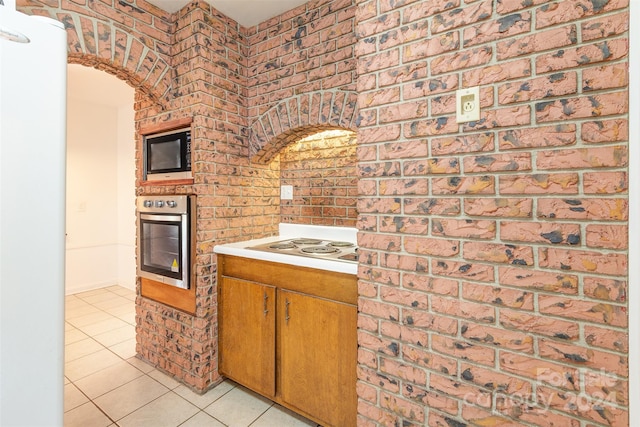 kitchen featuring brick wall, stainless steel oven, light tile patterned floors, and built in microwave