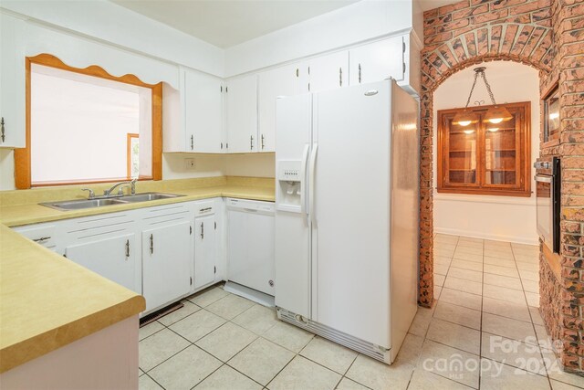 kitchen with light tile patterned flooring, white cabinets, white appliances, brick wall, and sink