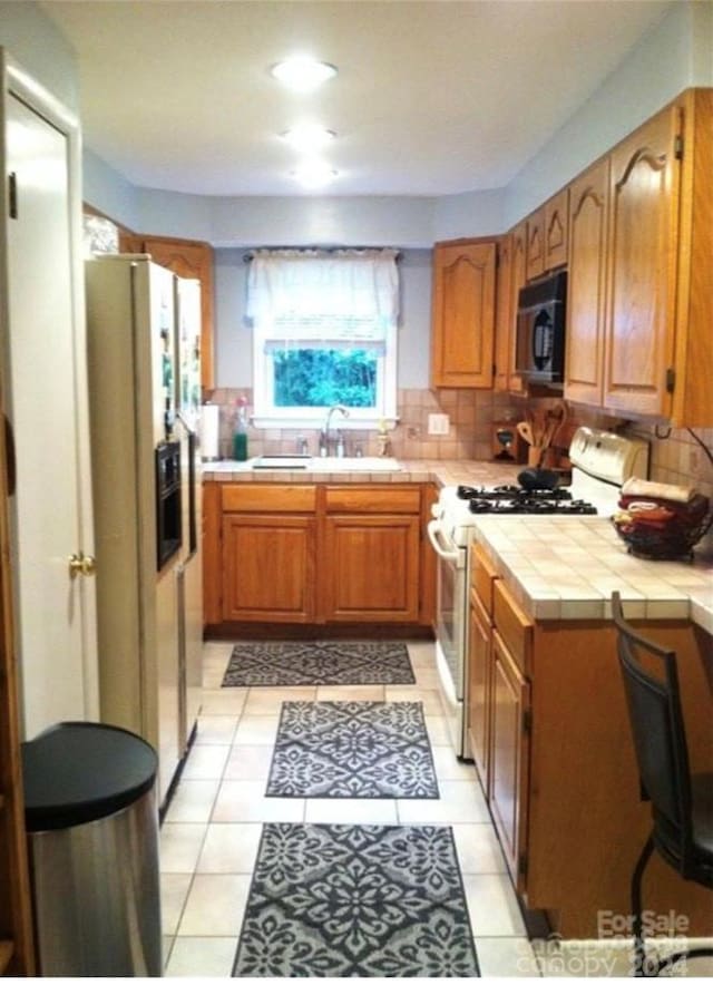 kitchen featuring tile countertops, sink, decorative backsplash, white gas stove, and fridge with ice dispenser