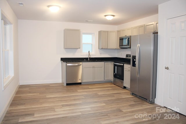 kitchen with dark countertops, a sink, light wood-style flooring, appliances with stainless steel finishes, and visible vents