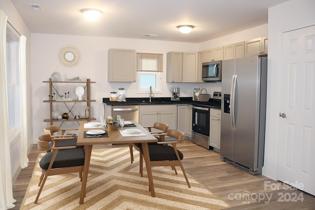 kitchen with light wood finished floors, dark countertops, visible vents, a sink, and appliances with stainless steel finishes