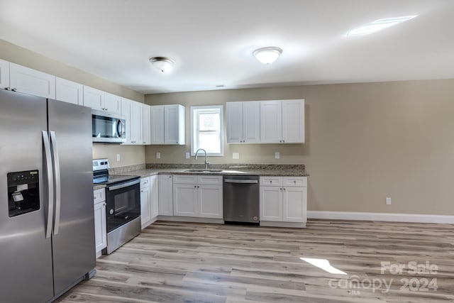 kitchen featuring light wood-type flooring, white cabinets, appliances with stainless steel finishes, stone countertops, and sink