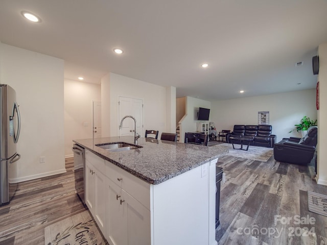 kitchen with wood finished floors, stone counters, stainless steel appliances, a sink, and white cabinetry