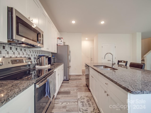 kitchen with a kitchen island with sink, a sink, tasteful backsplash, stainless steel appliances, and white cabinets