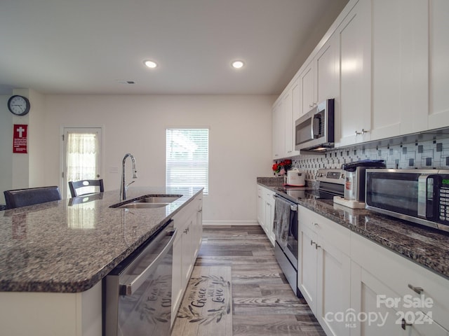 kitchen with tasteful backsplash, dark stone counters, appliances with stainless steel finishes, white cabinetry, and a sink