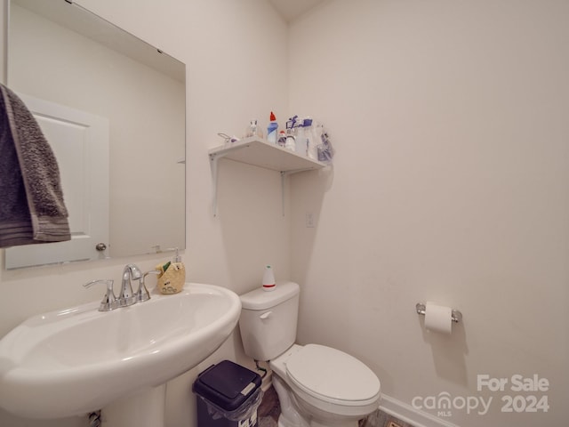 half bathroom featuring toilet, baseboards, and a sink