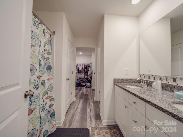 full bath with curtained shower, a walk in closet, double vanity, wood finished floors, and a sink