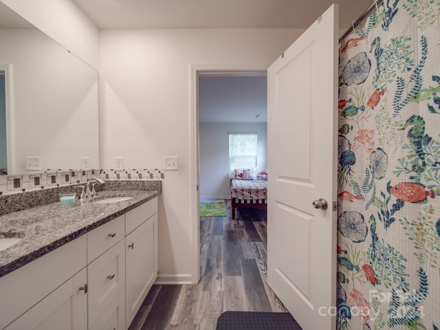 bathroom with wood finished floors, baseboards, double vanity, a sink, and ensuite bathroom