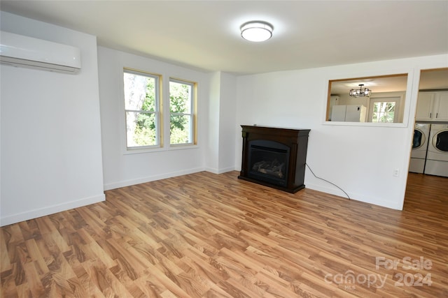 unfurnished living room with a wall unit AC, washing machine and dryer, and light wood-type flooring