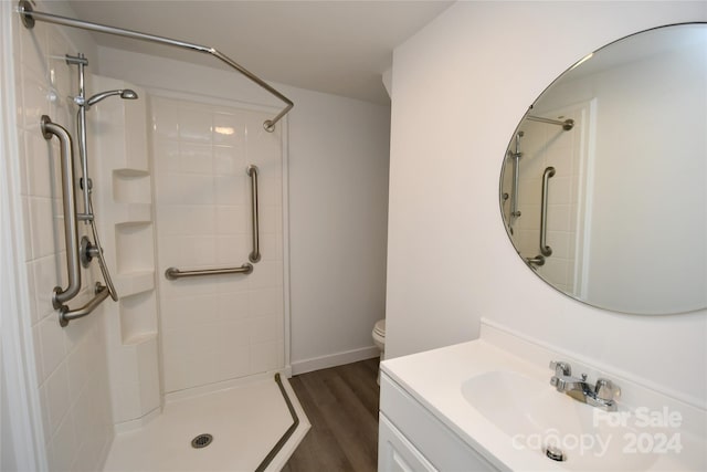 bathroom featuring wood-type flooring, tiled shower, vanity, and toilet