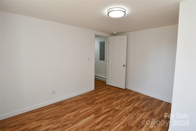 unfurnished room featuring hardwood / wood-style floors, a baseboard radiator, and electric panel