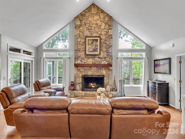 living room featuring light wood-type flooring, high vaulted ceiling, a stone fireplace, and a wealth of natural light