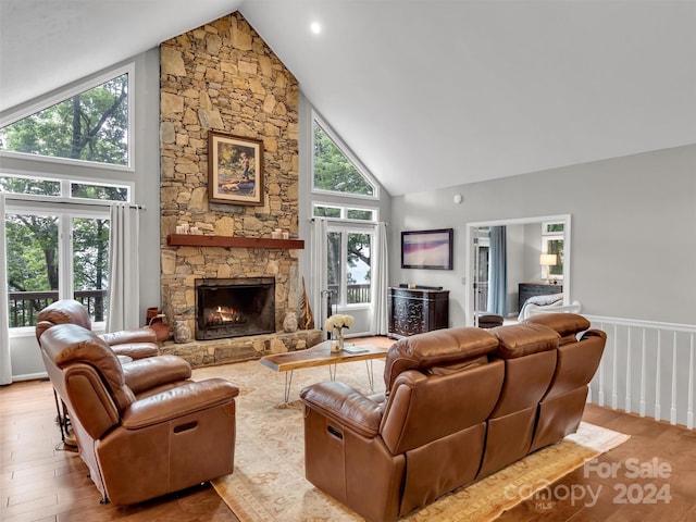 living room featuring hardwood / wood-style floors, high vaulted ceiling, plenty of natural light, and a stone fireplace