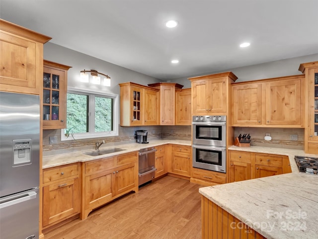 kitchen featuring light stone countertops, appliances with stainless steel finishes, light hardwood / wood-style floors, sink, and decorative backsplash