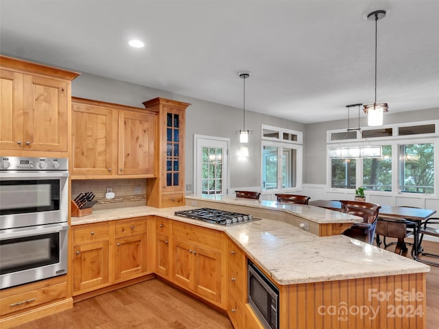 kitchen with a healthy amount of sunlight, backsplash, appliances with stainless steel finishes, and light hardwood / wood-style floors