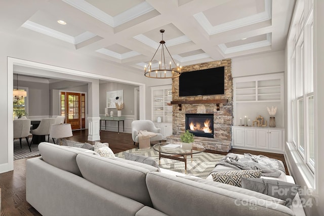 living room with built in shelves, an inviting chandelier, dark hardwood / wood-style floors, and a stone fireplace