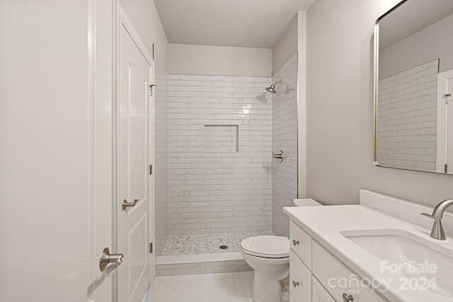 bathroom with tile patterned flooring, vanity, toilet, and a tile shower