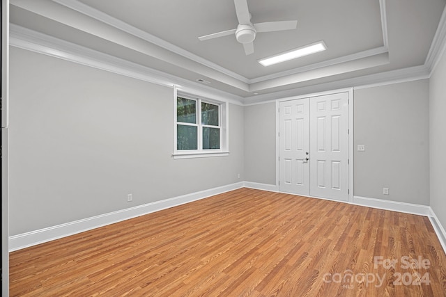 unfurnished bedroom with a raised ceiling, ceiling fan, light wood-type flooring, ornamental molding, and a closet