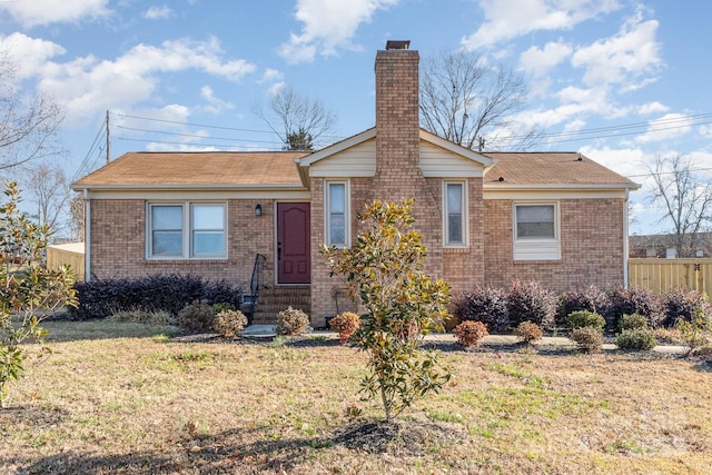 view of front of house with brick siding, a chimney, a front lawn, and fence