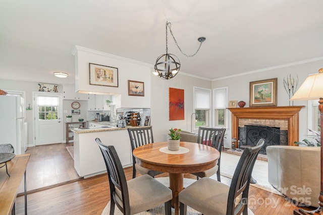 dining area featuring light wood-type flooring, a notable chandelier, a fireplace, and crown molding