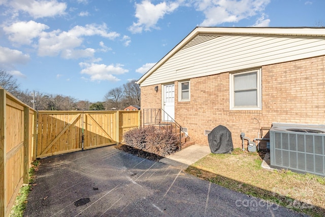 view of side of home with a gate, fence, cooling unit, and brick siding