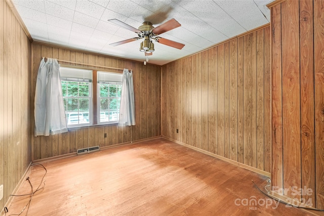 unfurnished room with hardwood / wood-style flooring, wooden walls, and ceiling fan