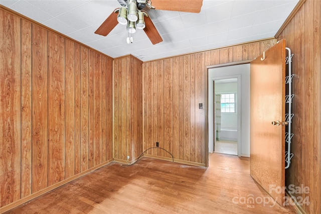 empty room featuring wooden walls, light hardwood / wood-style floors, and ceiling fan