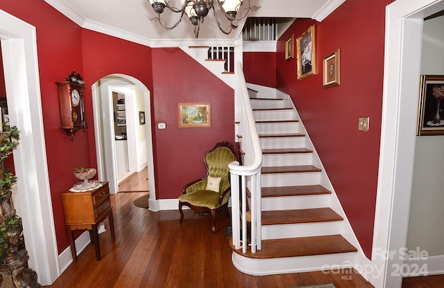 stairway with dark hardwood / wood-style flooring, ornamental molding, and an inviting chandelier