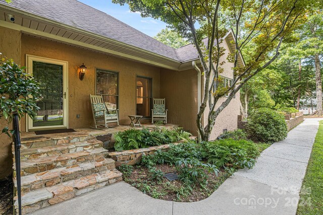 property entrance with covered porch, stucco siding, and a shingled roof