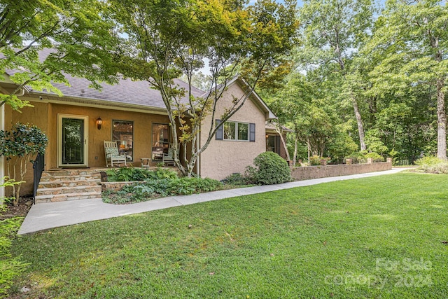 single story home with a shingled roof, a front yard, and stucco siding