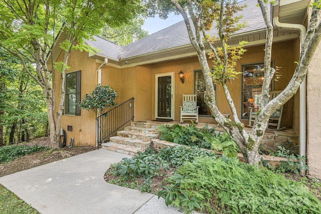 doorway to property with stucco siding and roof with shingles