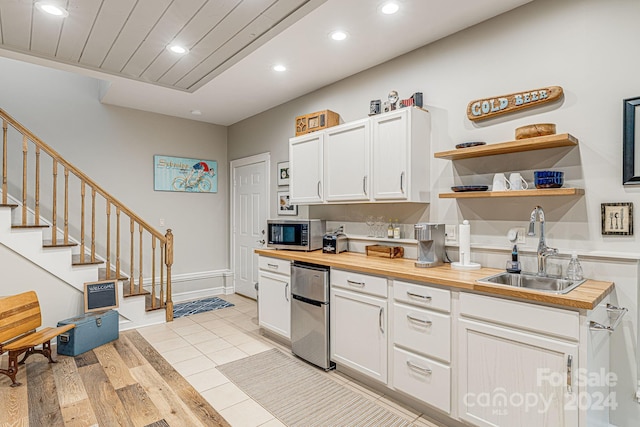 kitchen featuring recessed lighting, a sink, white cabinets, stainless steel microwave, and butcher block counters