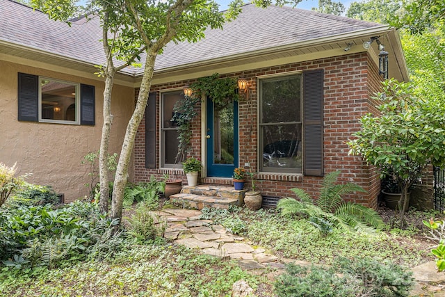 property entrance with brick siding, roof with shingles, and stucco siding