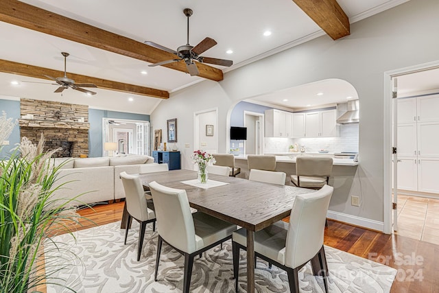 dining space featuring arched walkways, ornamental molding, a fireplace, and light wood finished floors