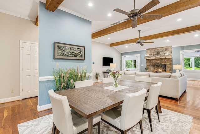 dining space featuring a stone fireplace, crown molding, light wood-style flooring, and baseboards