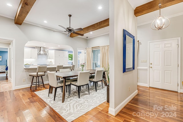 dining space featuring baseboards, light wood-type flooring, arched walkways, and beam ceiling