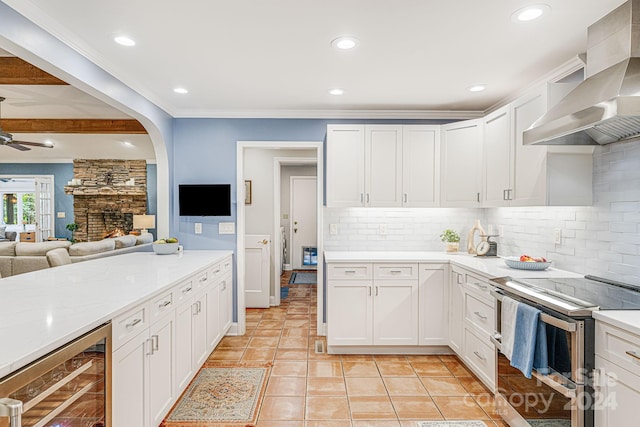 kitchen with backsplash, wall chimney range hood, wine cooler, stainless steel range with electric cooktop, and a ceiling fan