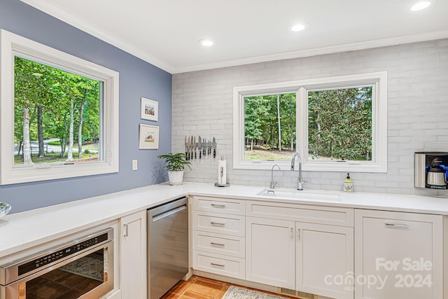 kitchen with light stone countertops, white cabinetry, a sink, stainless steel dishwasher, and crown molding