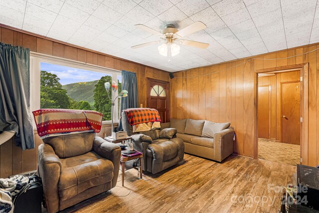 living room with wood-type flooring, wood walls, and ceiling fan