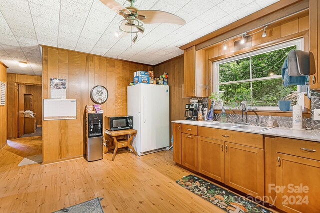 kitchen featuring white fridge, light hardwood / wood-style flooring, wooden walls, ceiling fan, and sink