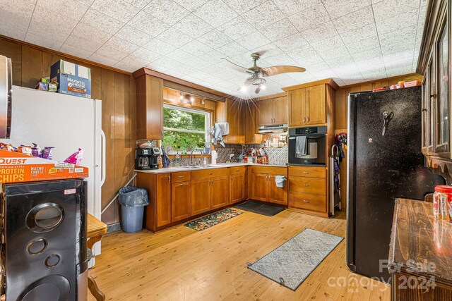 kitchen with black appliances, ceiling fan, light wood-type flooring, sink, and range hood