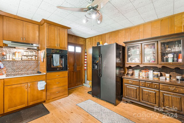 kitchen featuring light hardwood / wood-style floors, black appliances, ceiling fan, and wood walls