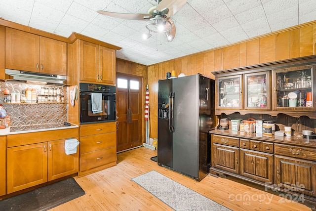 kitchen with ceiling fan, light hardwood / wood-style flooring, wooden walls, and black appliances