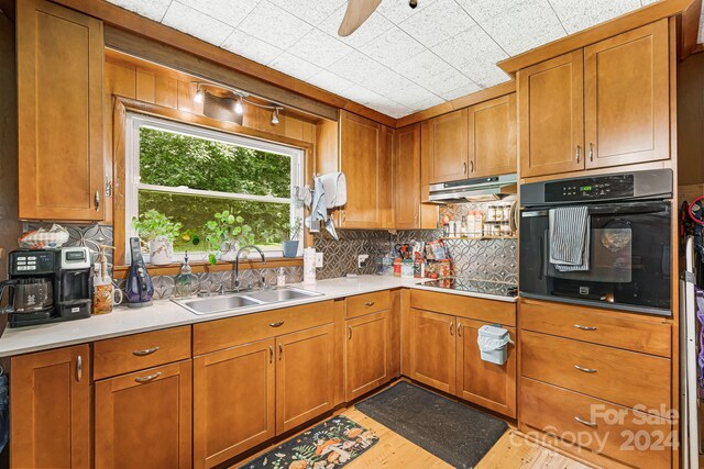 kitchen featuring light wood-type flooring, ceiling fan, black appliances, decorative backsplash, and sink