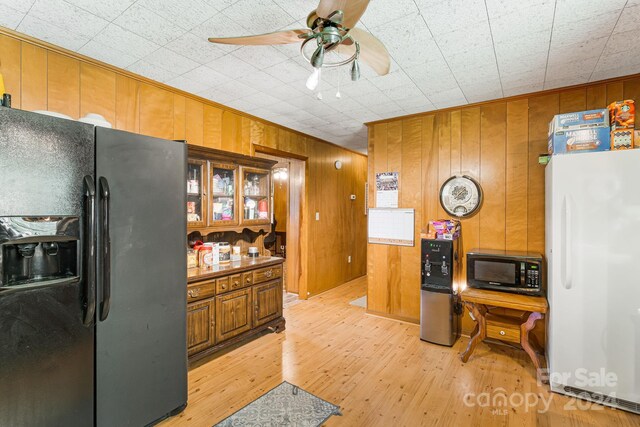 kitchen featuring wooden walls, ceiling fan, black appliances, and light hardwood / wood-style floors