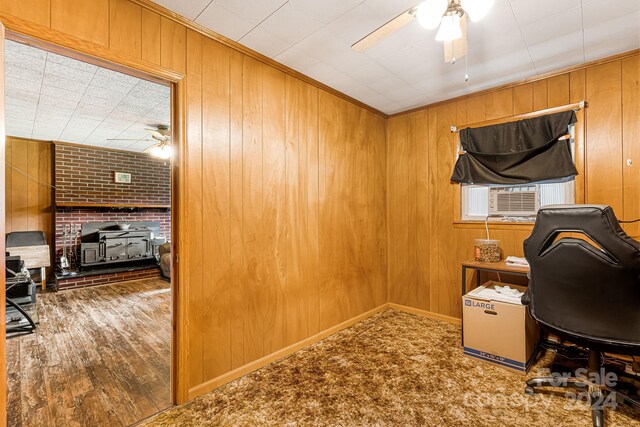 home office with a fireplace, hardwood / wood-style flooring, wooden walls, and ceiling fan