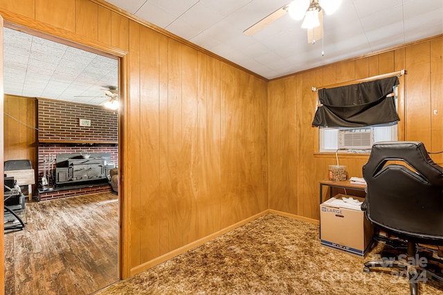 home office featuring a wood stove, wooden walls, and ceiling fan